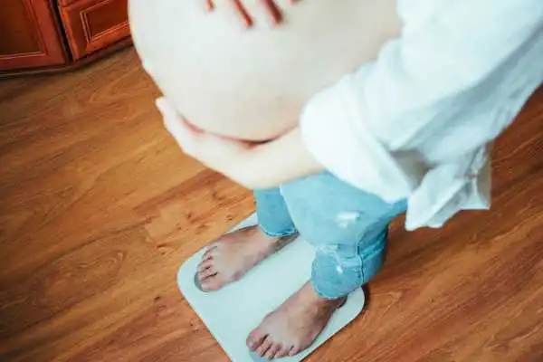 Image of woman weighing herself and experiencing weight gain through pregnancy Pollokshields